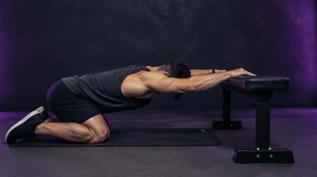 Kneeling Bench Lat Stretch: Man kneeling with both hands on a bench, hips back and chest sinking toward the floor