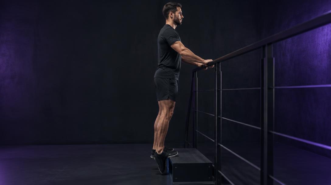 Loaded Step Stretch: Man standing with the balls of his feet on a step and heels dropped below it