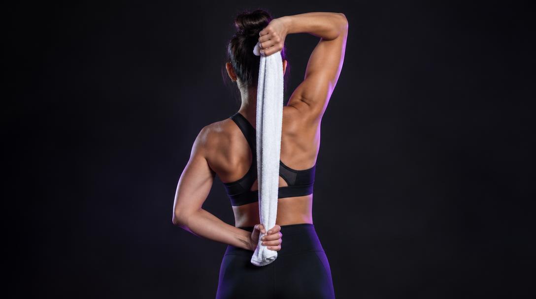 Towel-Assisted Triceps Stretch: Woman holding a towel behind her back, top hand overhead and bottom hand at the low back